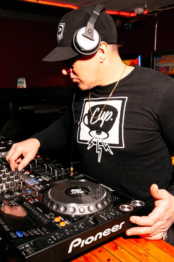Woofax — a DJ in a C.U.P long-sleeve on the CDJs